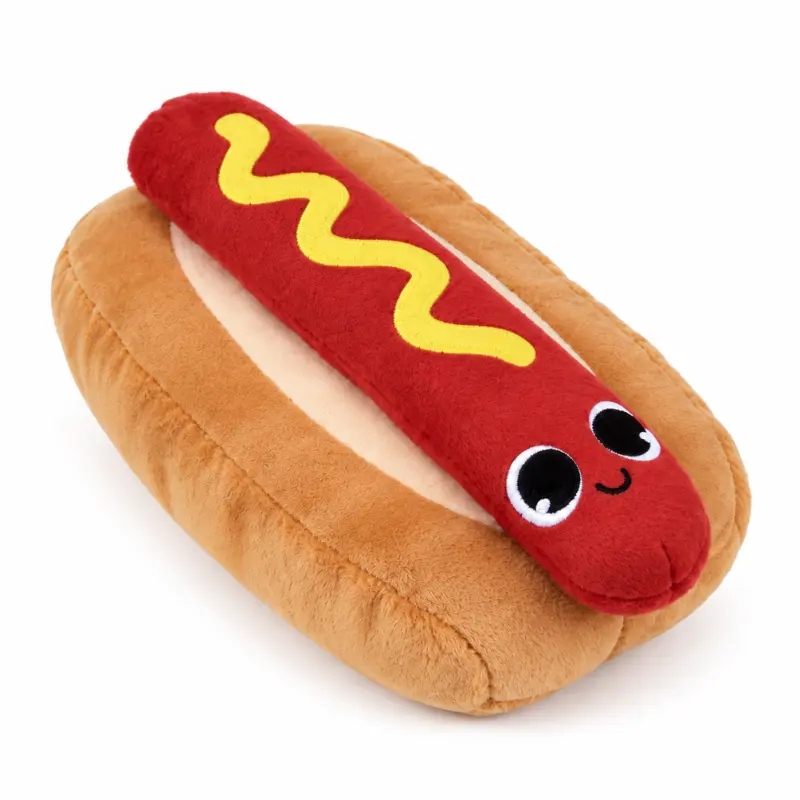 A cute dog plushie shaped like a hot dog, with a red sausage, yellow mustard stripe, tan bun, and embroidered smiling face.