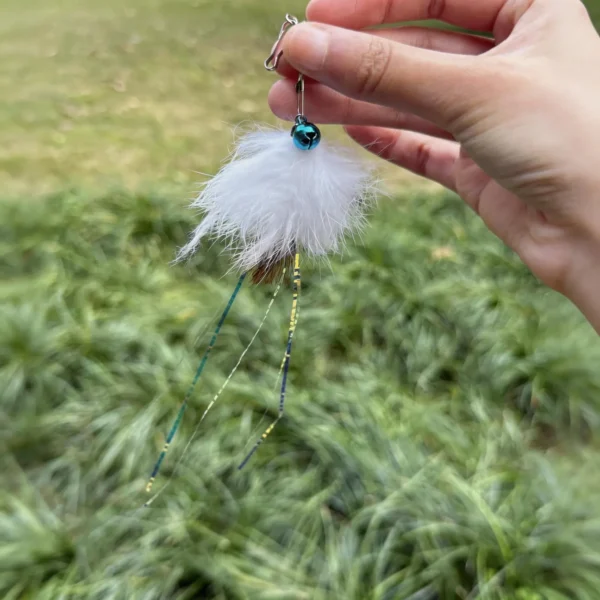 A hand holds a Jellyfish Rabbit and Deer Fur Cat Wand Replacement outdoors, showing the fluffy fur body, blue bell, and dangling shimmer ribbons.
