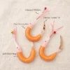 Material details of a handmade shrimp cat toy wand refill showing mesh shrimp shell, soft wool filling, chicken feather tail, and iridescent whiskers.
