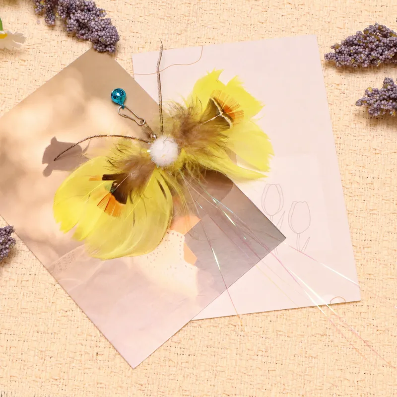 Yellow Butterfly Cat Toy Wand Replacement displayed on pastel art cards with layered feather wings, a blue bell, and iridescent trailing fibers.