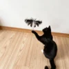 black-cat-swatting-cat-teaser-toy Black cat swatting a giant moth cat teaser toy with layered feather wings and dangling reflective strips during interactive play.