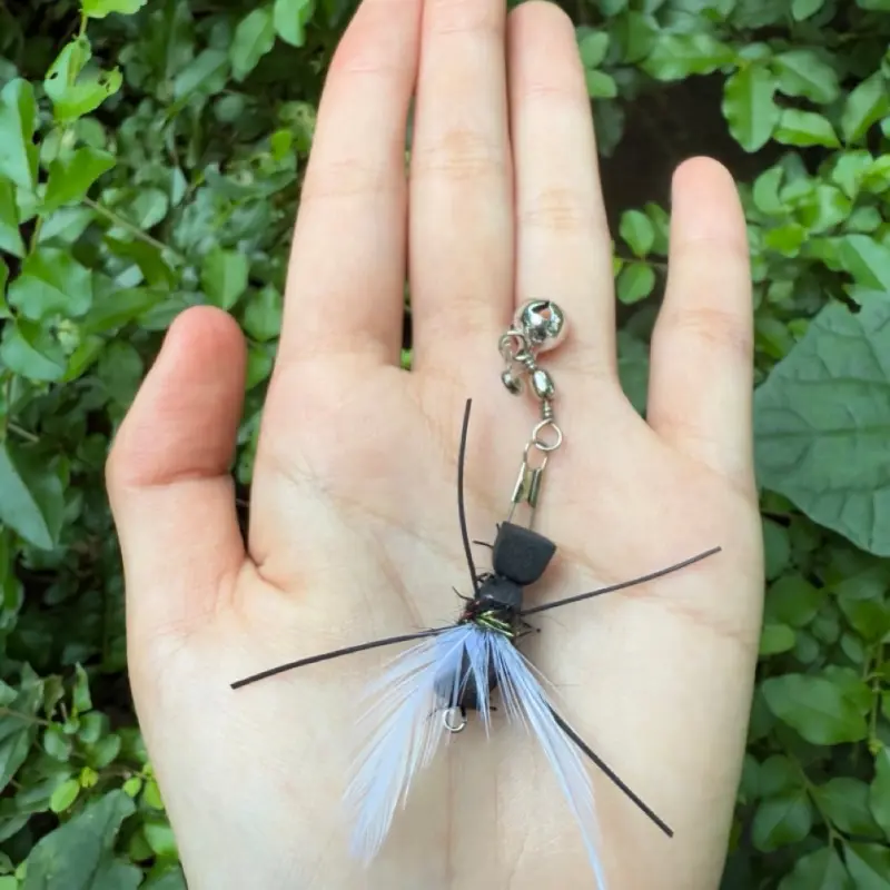 crawling-ant-cat-toy-wand-white-feather-outdoor-view White feather crawling ant cat toy wand attachment shown outdoors, featuring a small insect design that mimics prey movement for interactive play.