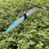 crinkle-film-dragonfly-cat-wand-toy-outdoors Blue Crinkle Film Dragonfly Cat Toy clipped to a black cat wand against green foliage.