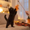 Black cat playing with a Halloween cat toy wand during interactive play with a pumpkin feather teaser