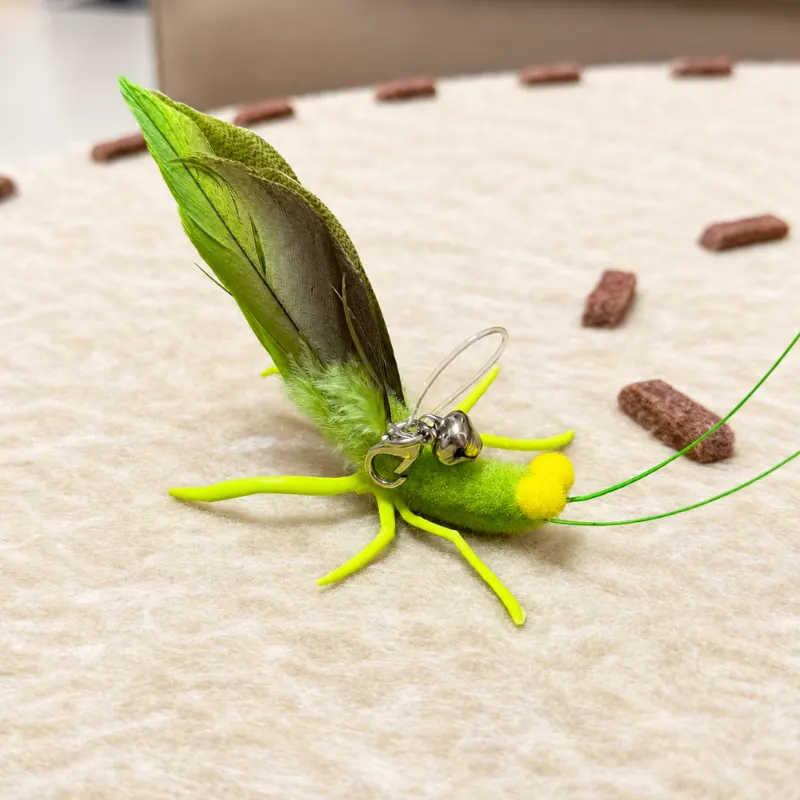 Grasshopper cat toy resting on the floor, designed for cats that like to hunt, stalk, and pounce.