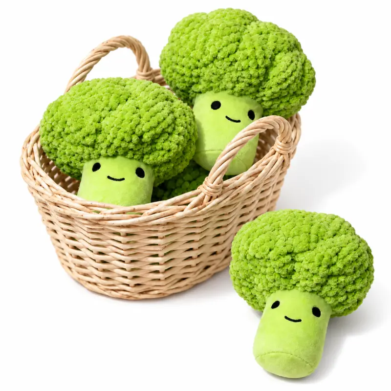 broccoli-plush-dog-toys-basket-display Three cute dog plushies shaped like smiling broccoli sit in and beside a wicker basket; these green squeaky plush dog toys have textured crowns.