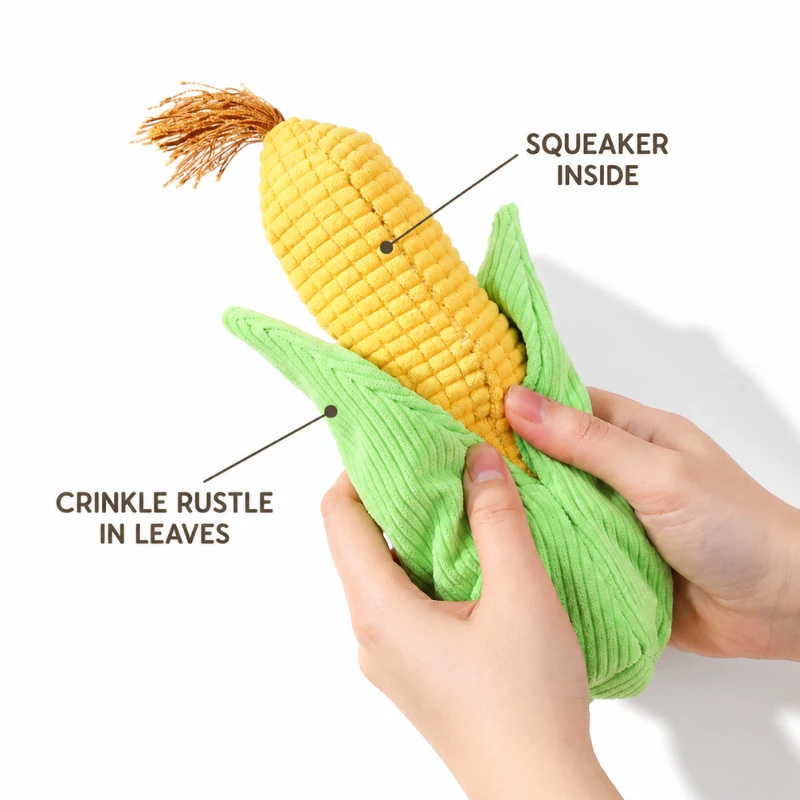 corn-plush-squeaker-crinkle-leaves Hands squeeze a corn-shaped plush squeaky dog toy, highlighting the squeaker inside the yellow cob and crinkle paper inside the green leaves.