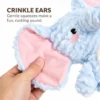 A hand squeezes the pink inner ear of the blue elephant dog toy to demonstrate its crinkle ears and the soft rustling sound they make.