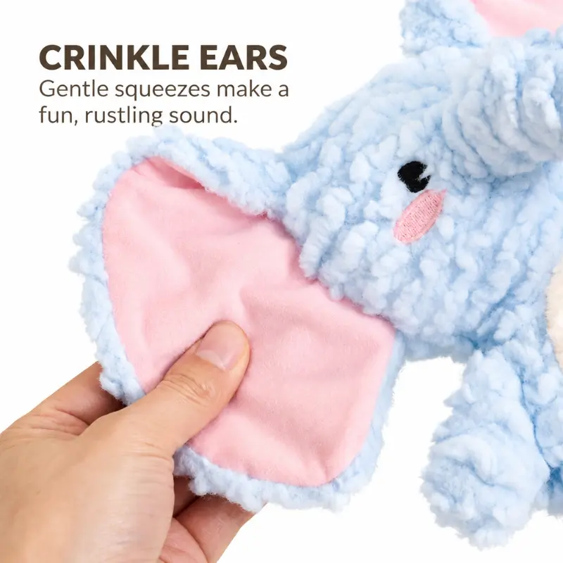A hand squeezes the pink inner ear of the blue elephant dog toy to demonstrate its crinkle ears and the soft rustling sound they make.